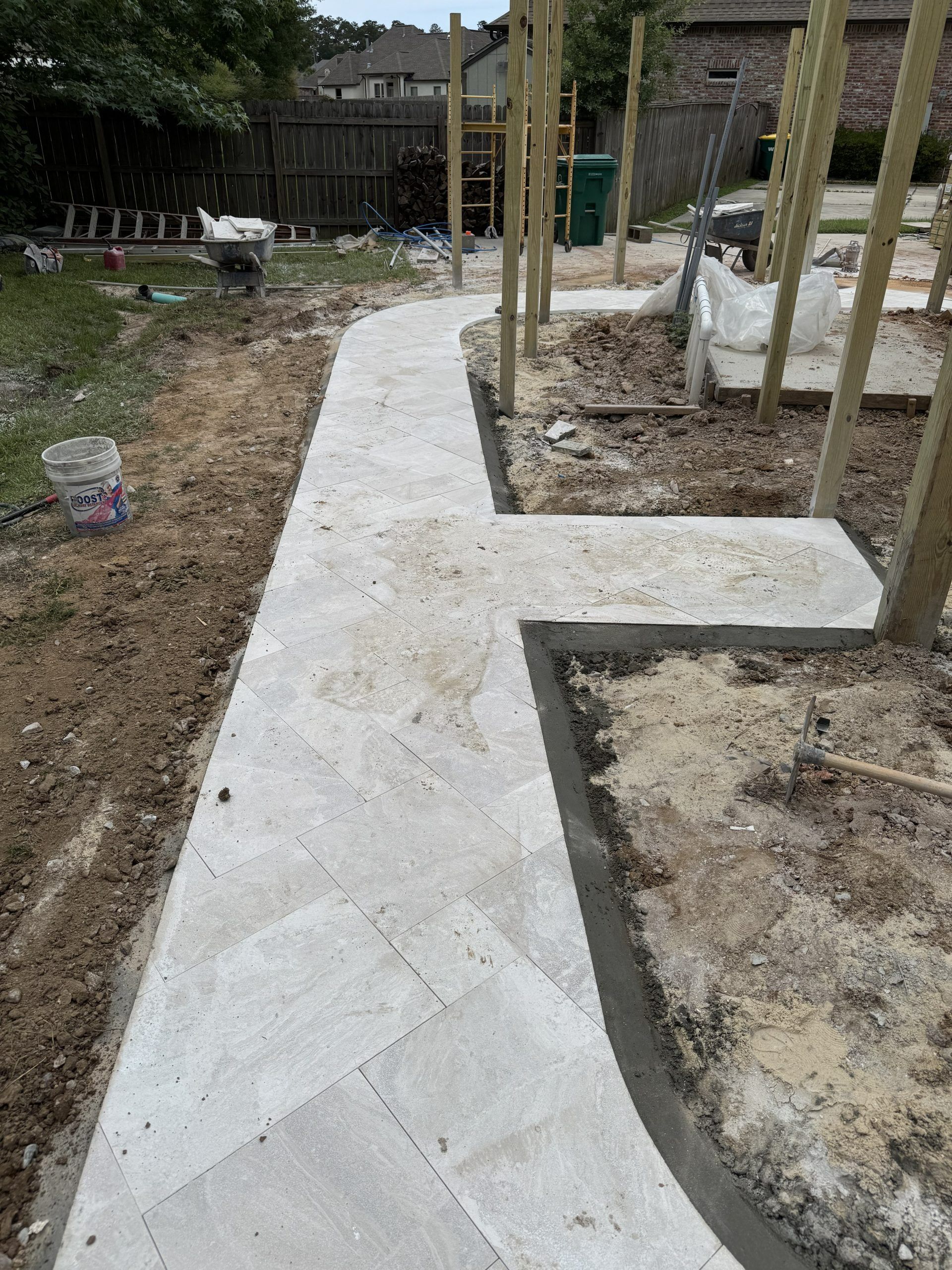 Fresh concrete garden walkway curving between soil beds and wooden posts in an outdoor yard