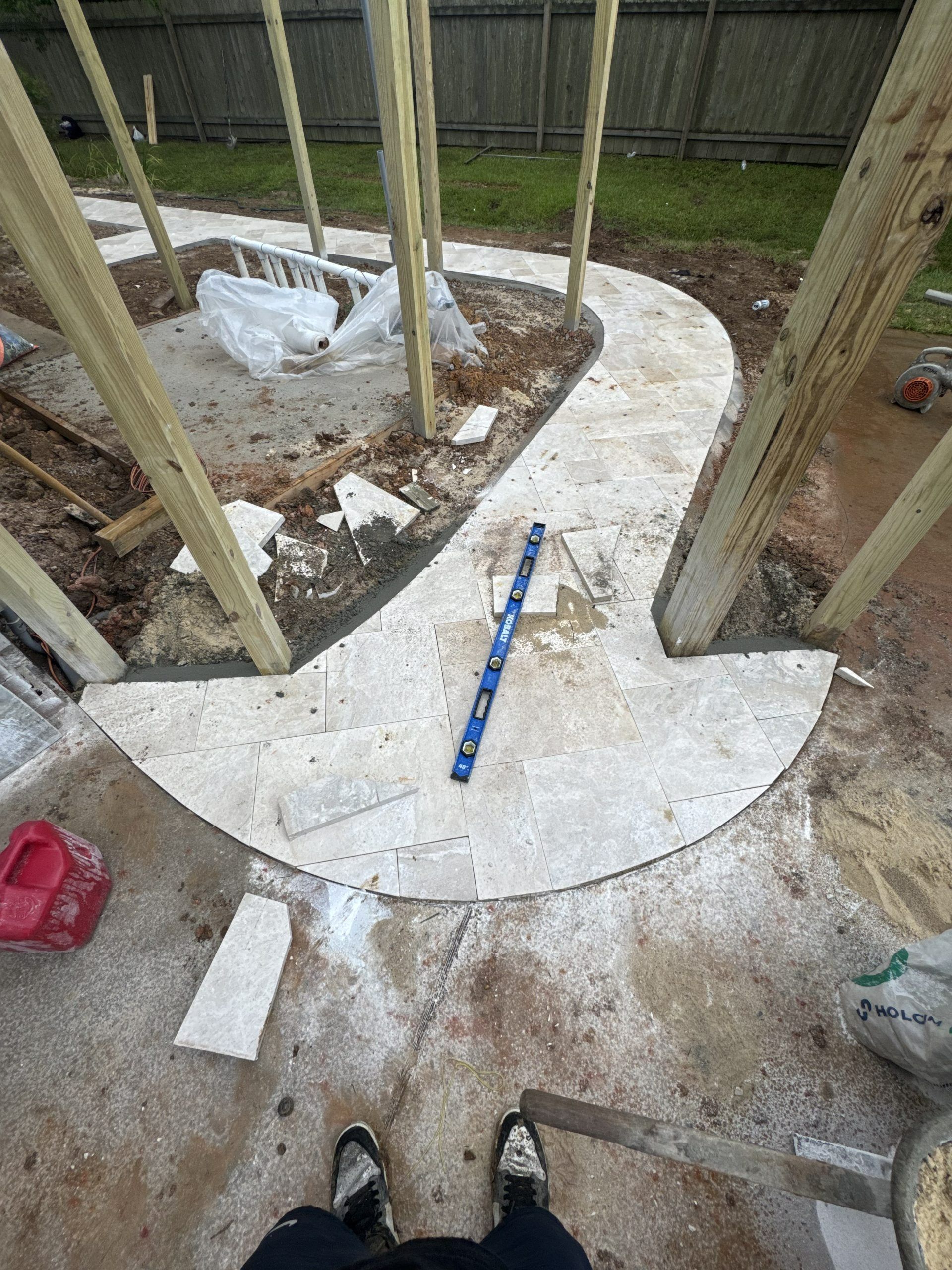 Curved concrete walkway under construction with wooden posts, tools, and dirt along the edges