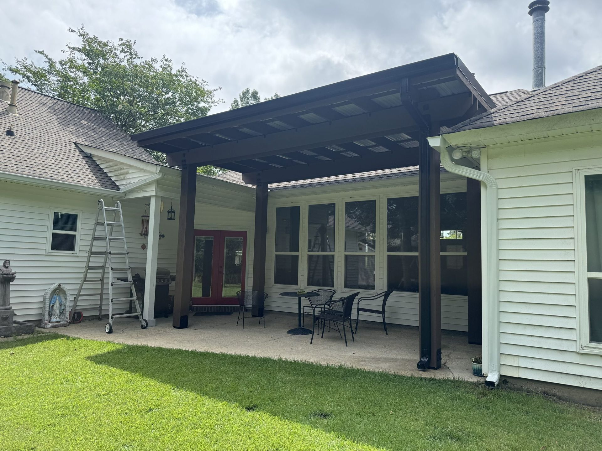 White house patio with dark pergola, glass doors, and outdoor seating on a green lawn