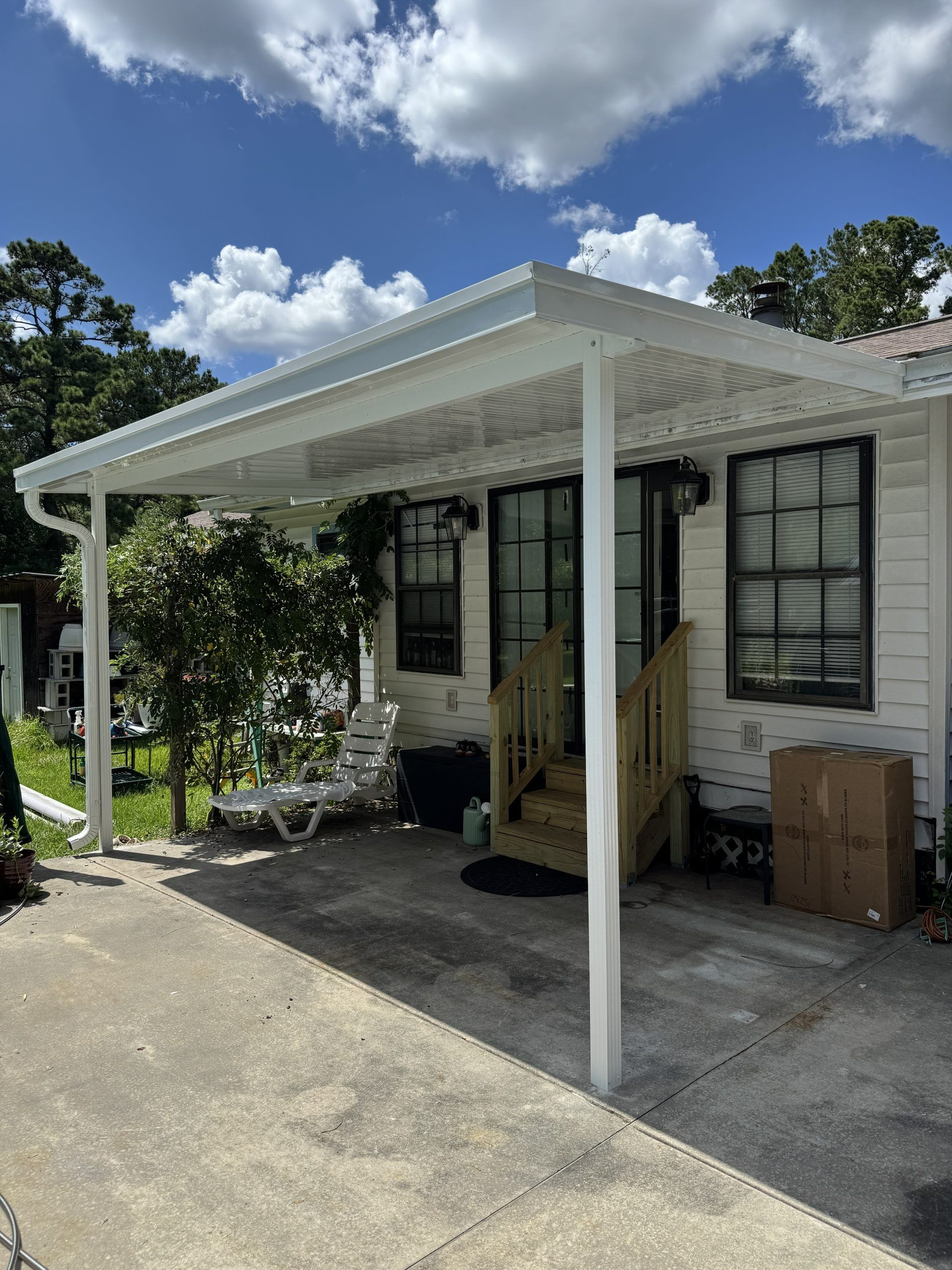 Small house porch with white awning, black-trimmed windows, and potted plants beside a driveway
