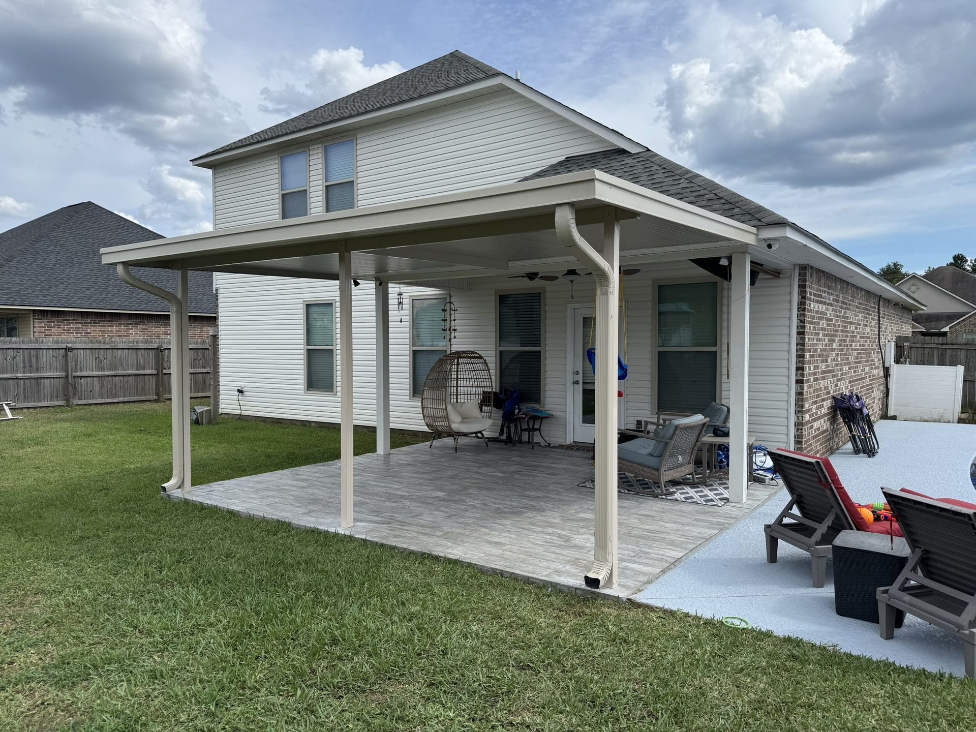 Backyard patio with a covered pergola, outdoor furniture, and a two-story house beside a grassy lawn