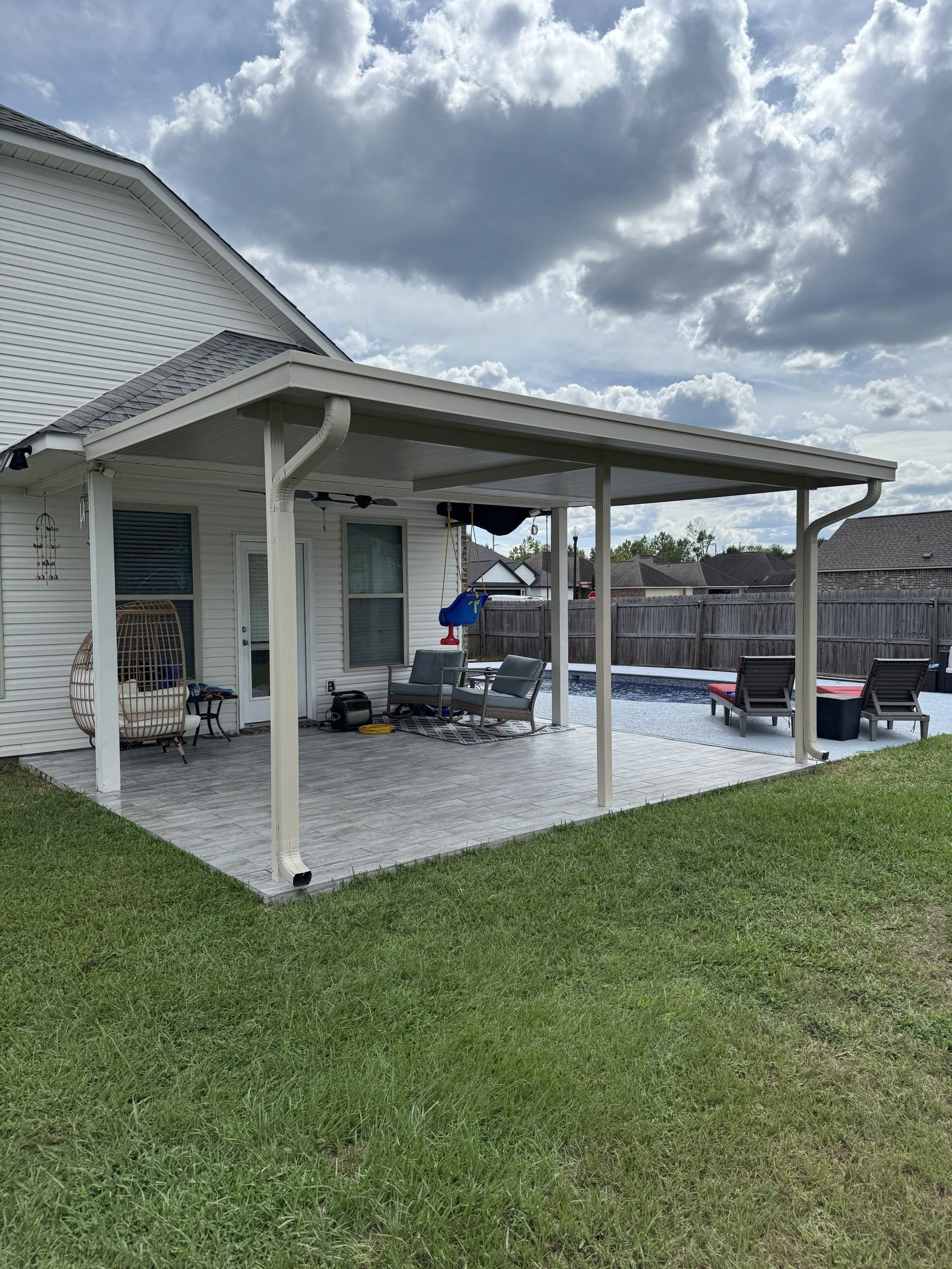 Covered patio beside white house with wicker chairs, grill, and lake view under cloudy sky