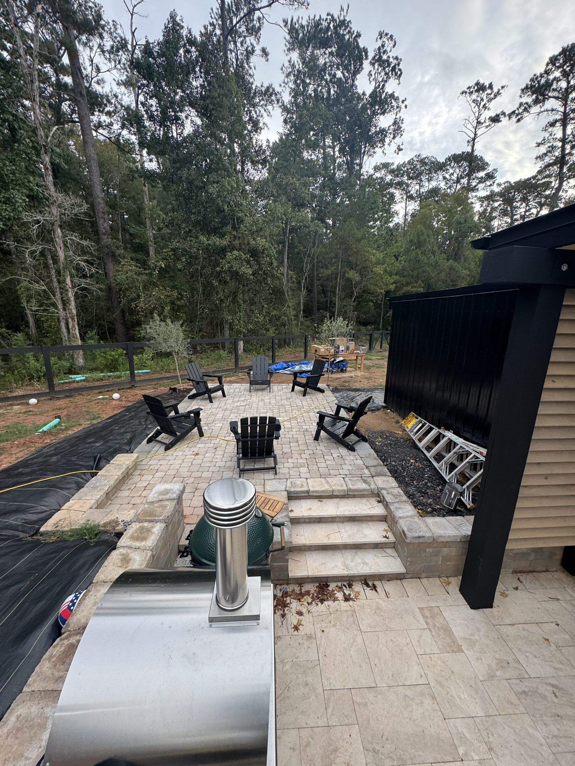 Outdoor patio with concrete steps, black chairs, and a wooded garden setting