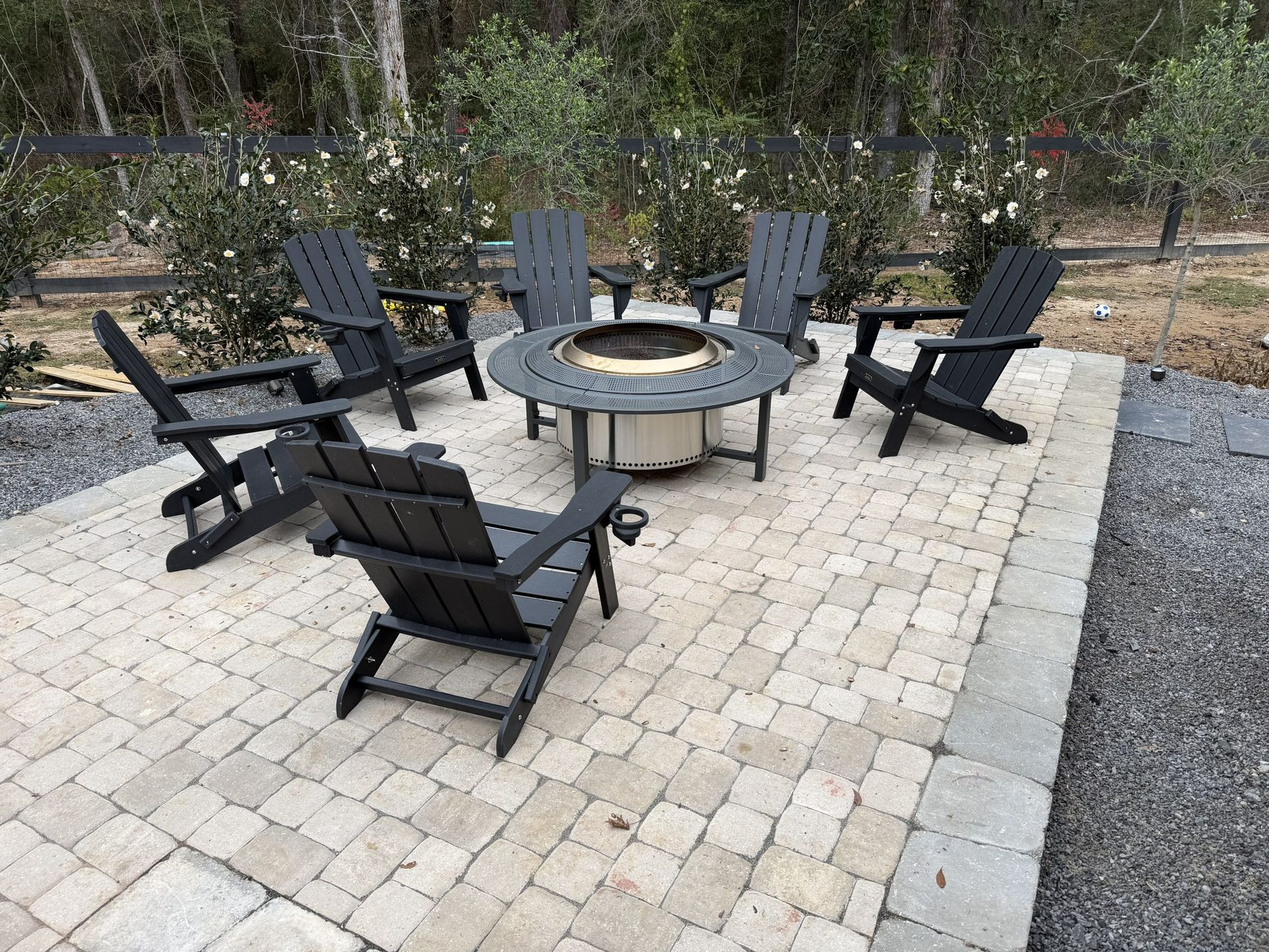 Outdoor patio with black Adirondack chairs around a circular fire pit on a stone paver площадка