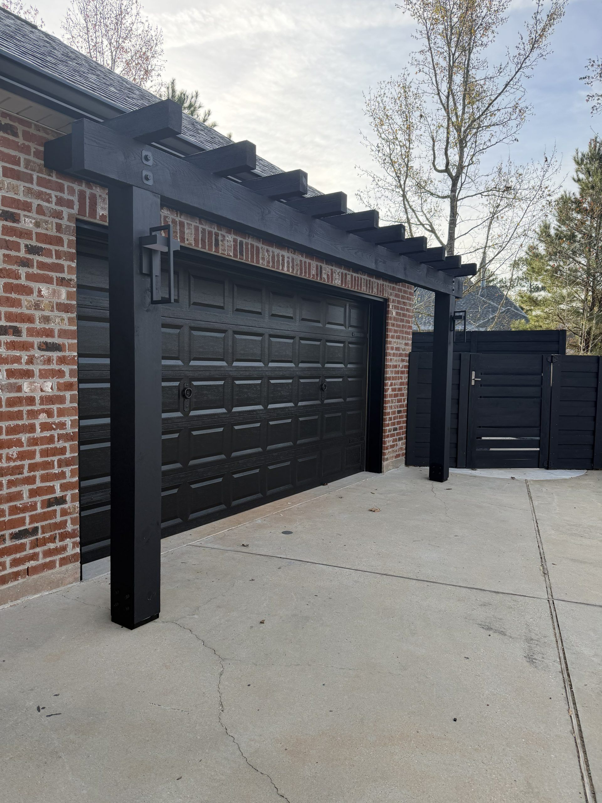 Brick house exterior with black garage doors, black posts, and a concrete driveway under a cloudy sky