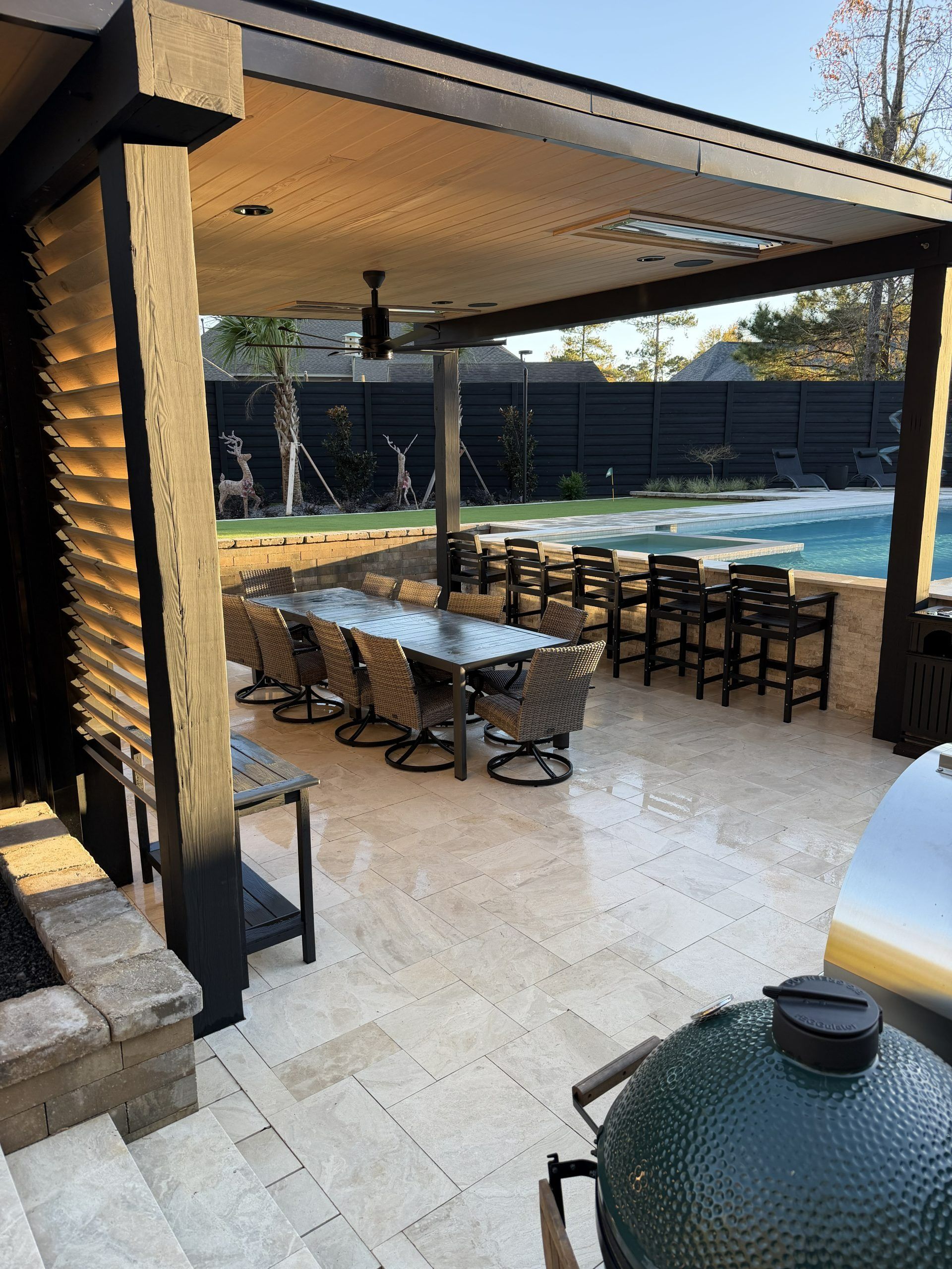 Covered patio with outdoor dining table and bar stools beside a backyard swimming pool.