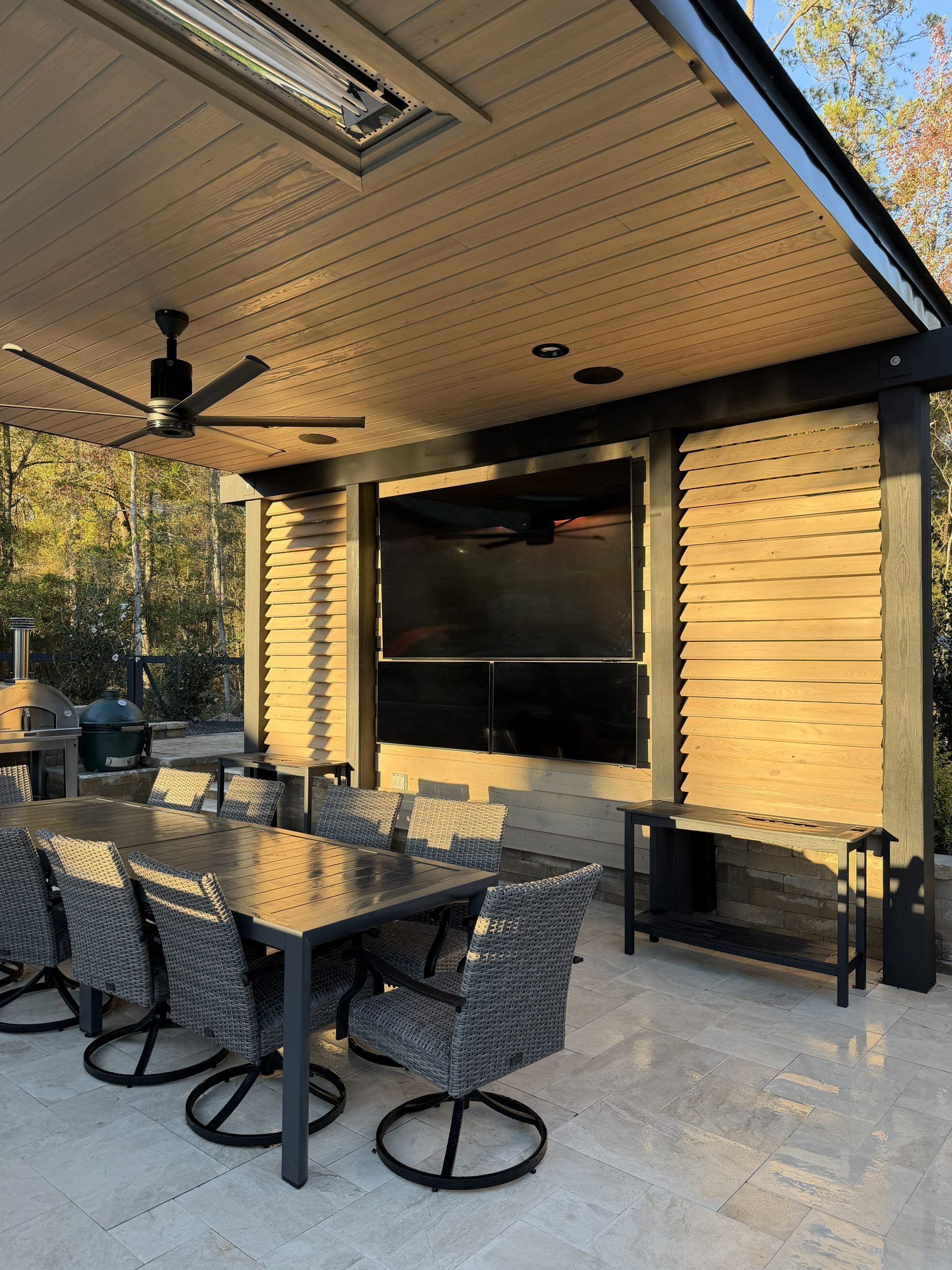 Outdoor patio with dining tables, chairs, and a ceiling fan under a covered pergola.