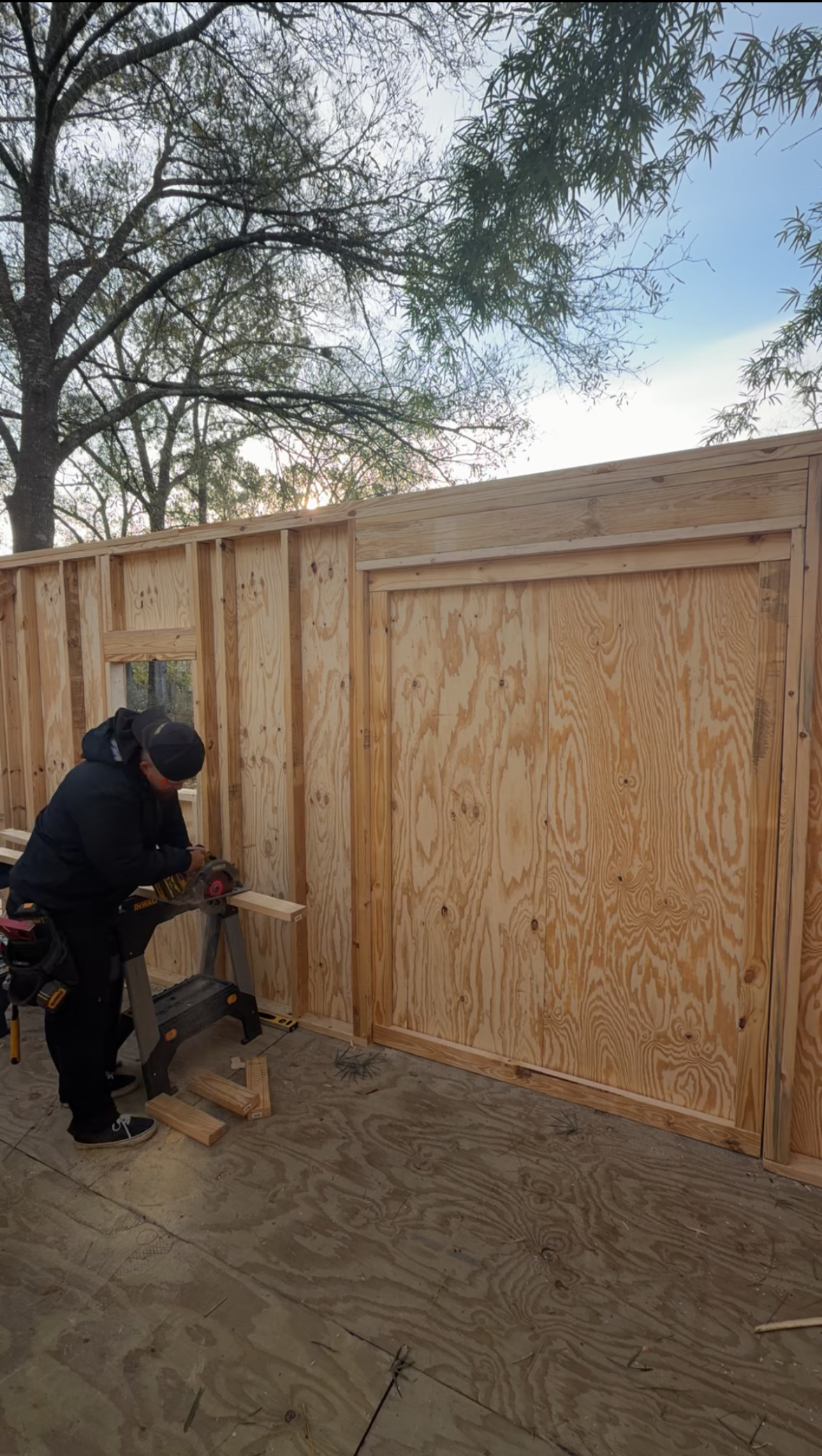 Worker using a tool near a plywood fence panel outdoors in daylight