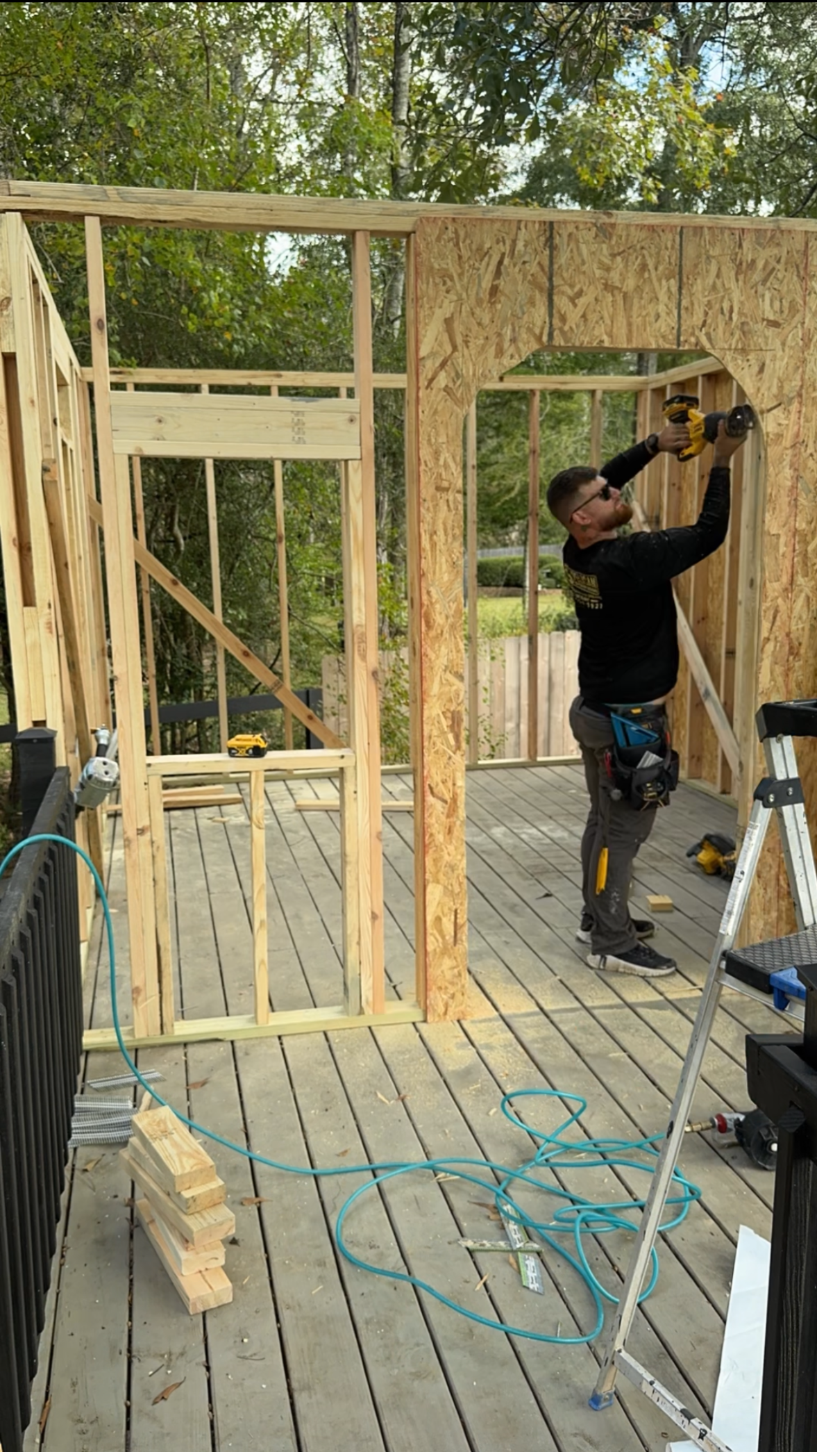 Framed wooden walls and doorway under construction, with a worker using a drill indoors.