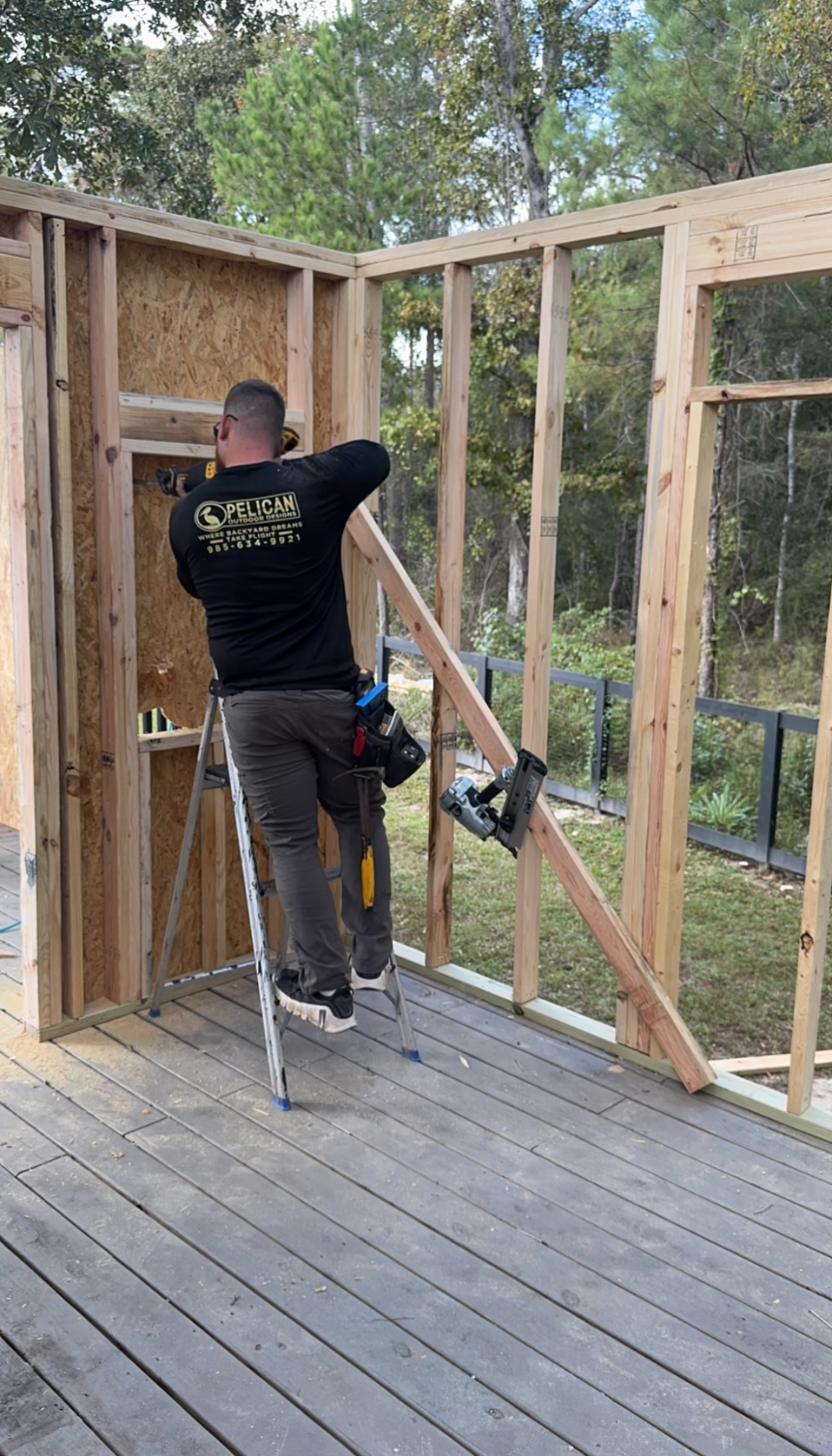 Worker using a ladder to frame a wooden wall inside an unfinished building