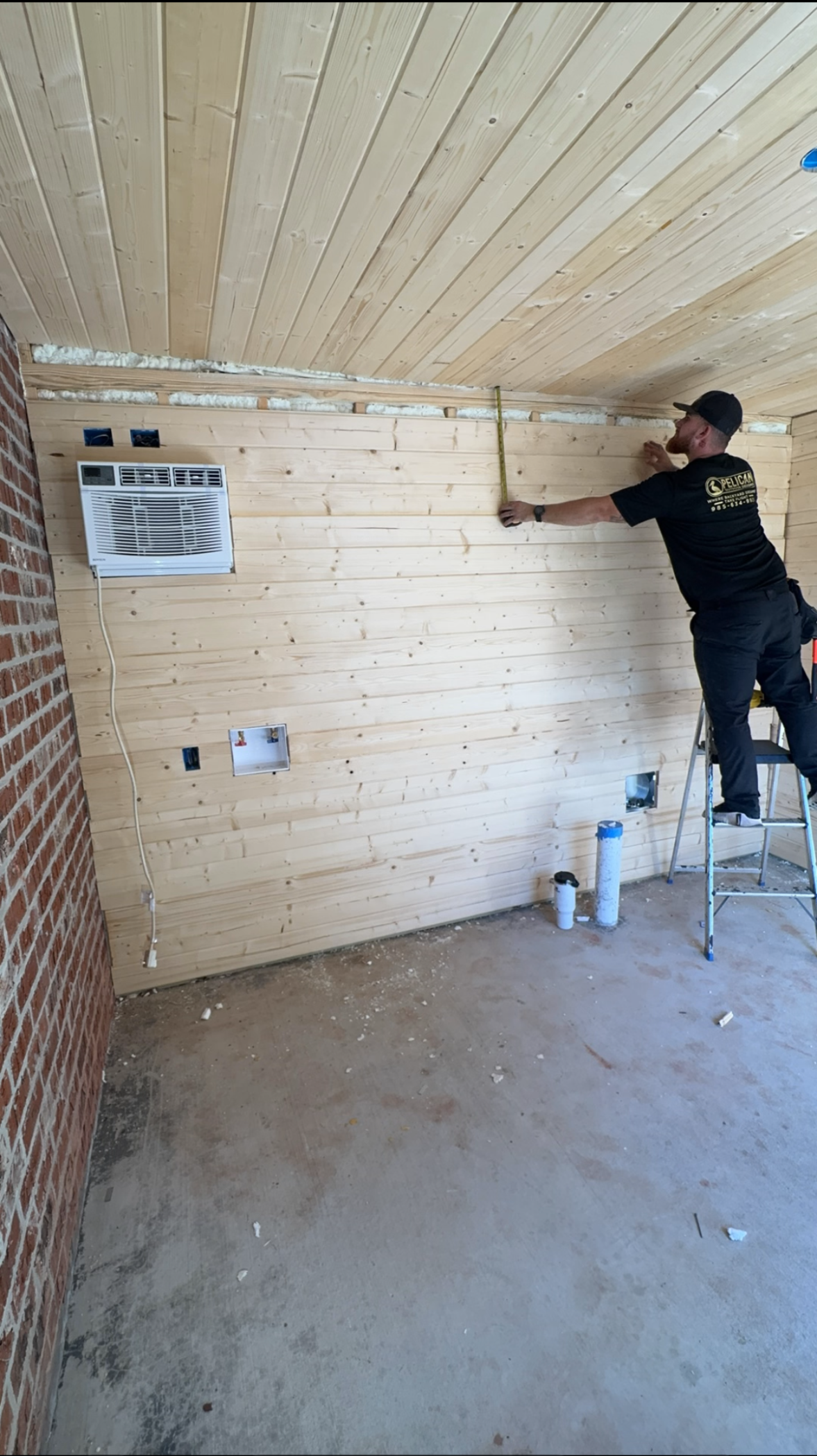 Worker painting a white brick wall in a small unfinished room