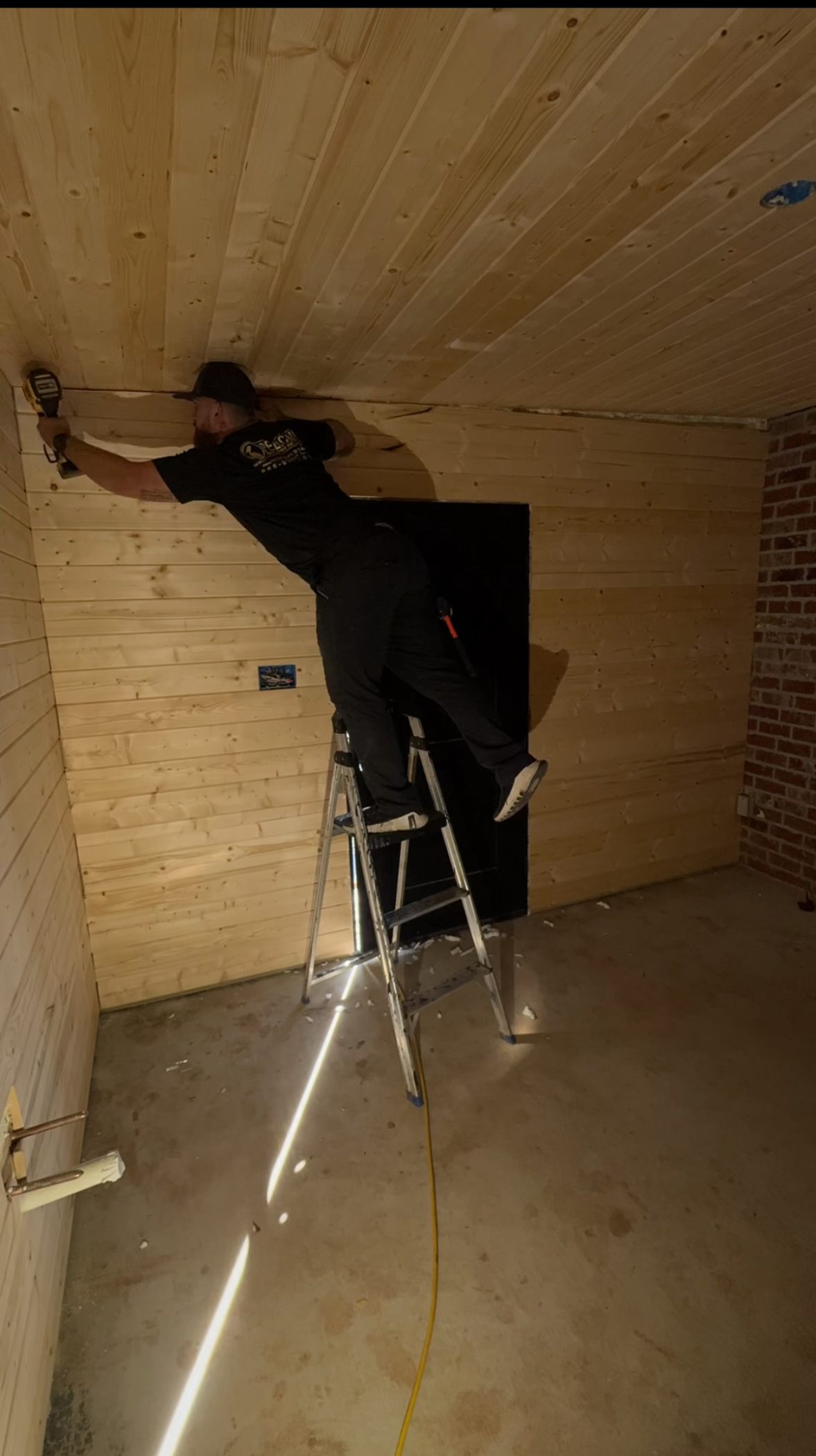 Person on a ladder painting a wooden ceiling in an unfinished room