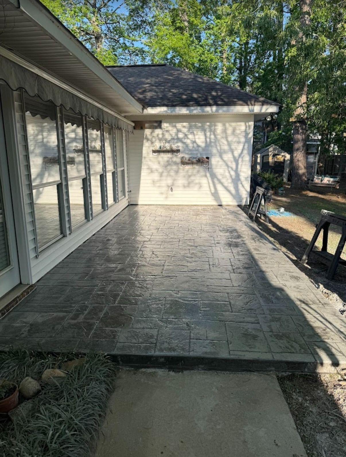 Stone patio beside a house with sliding glass doors and trees in the yard