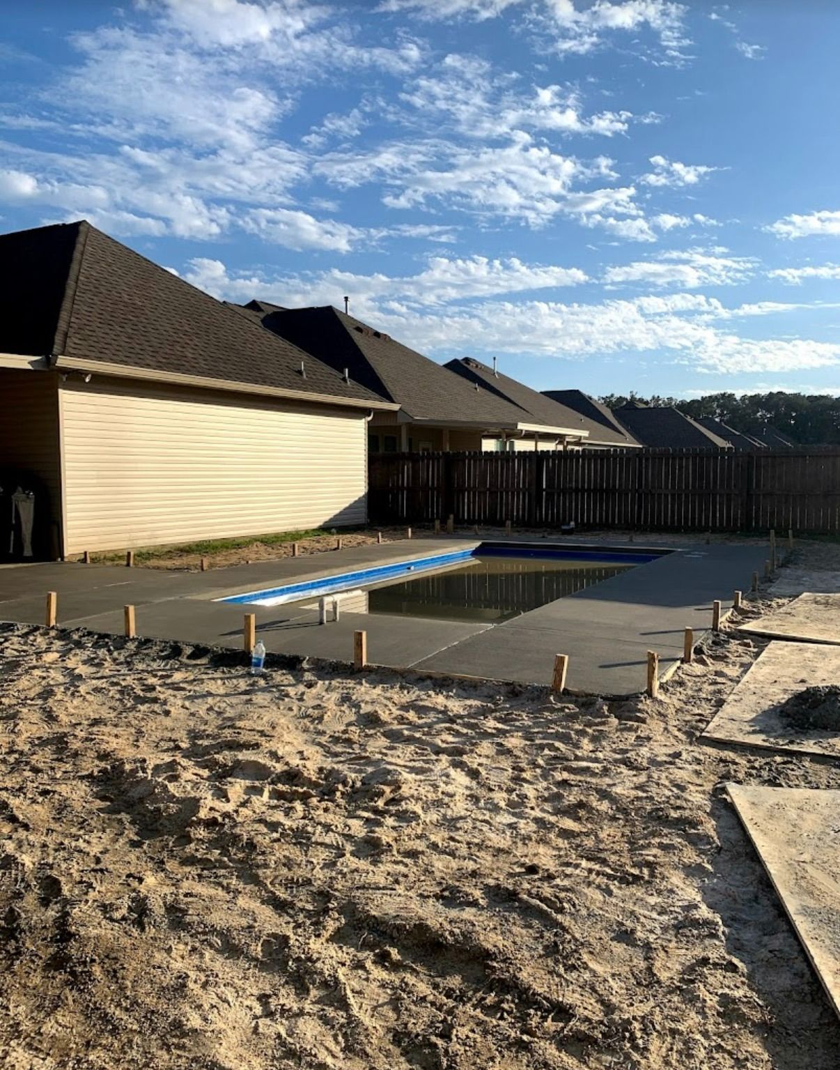 Backyard under construction with a partially poured concrete patio beside a wooden fence and houses