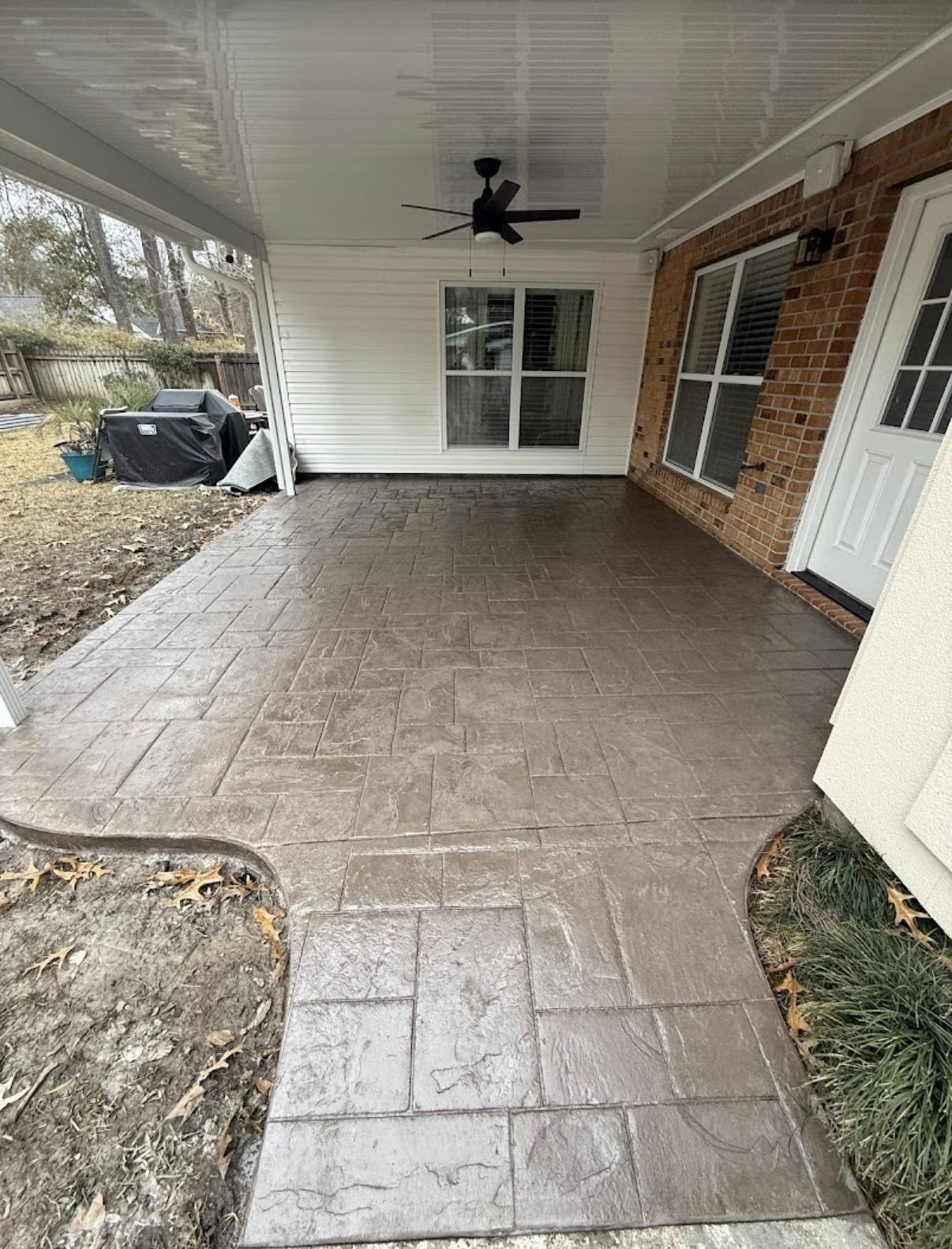 Covered front porch with stamped concrete floor, brick wall, white door, window, and ceiling fan