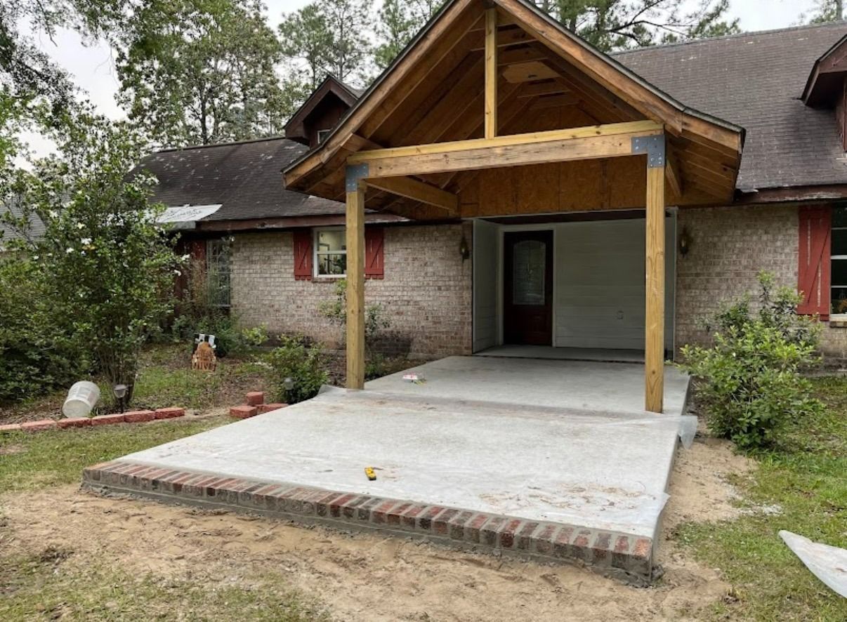 Rustic house entrance with a covered porch, concrete ramp, and landscaped yard