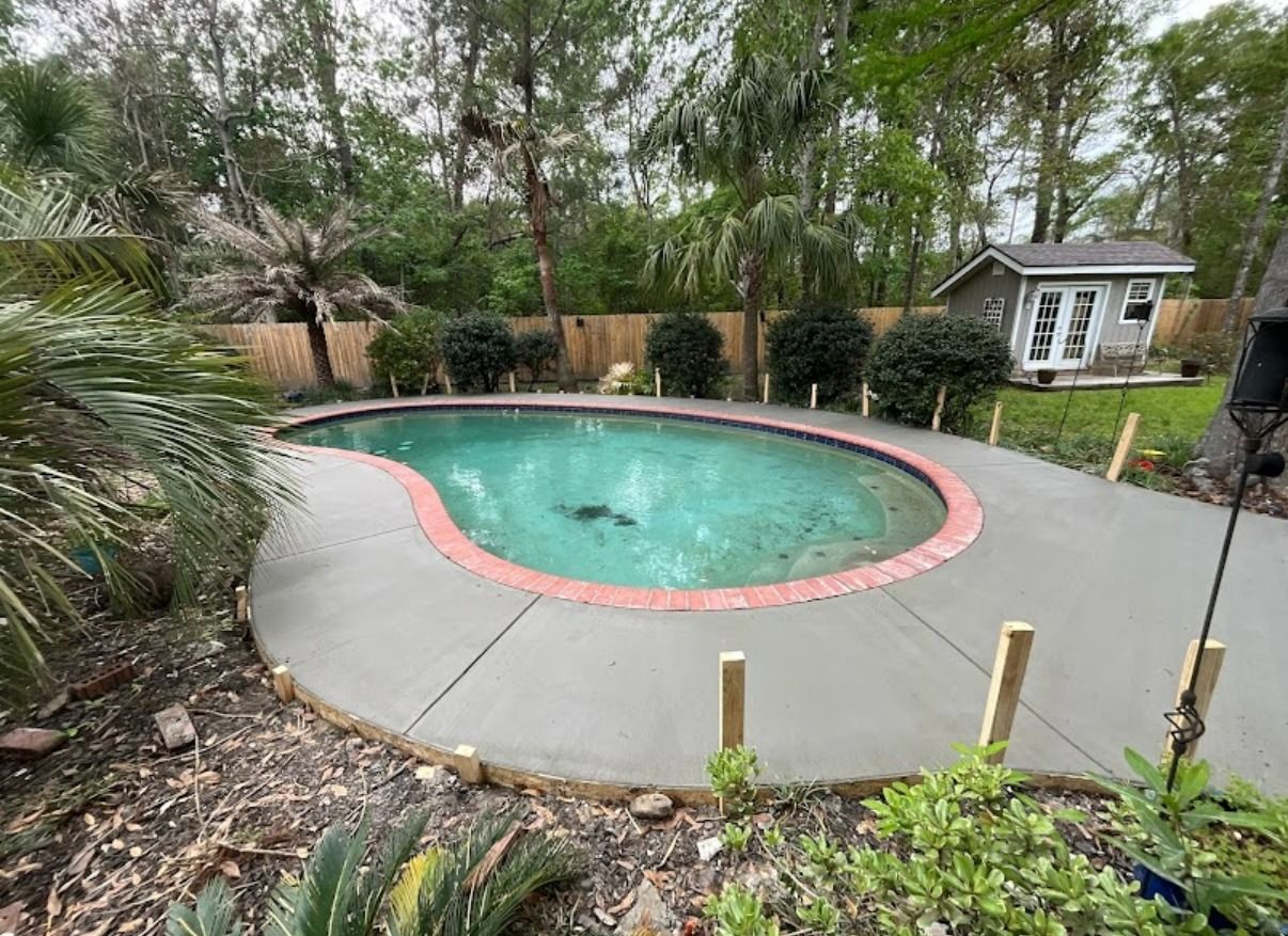 Backyard swimming pool with red edging, surrounded by concrete patio and greenery