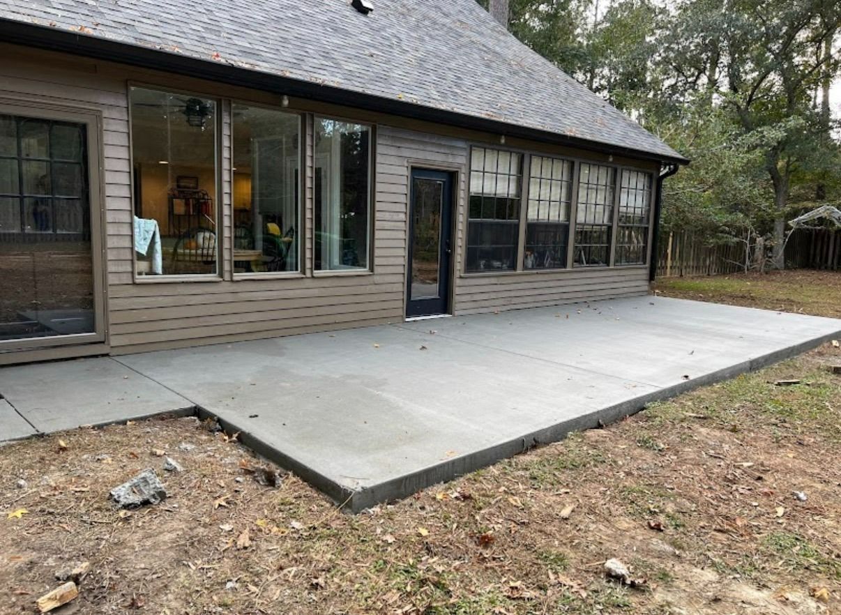 Modern house exterior with a large concrete patio and accessible walkway in a wooded yard