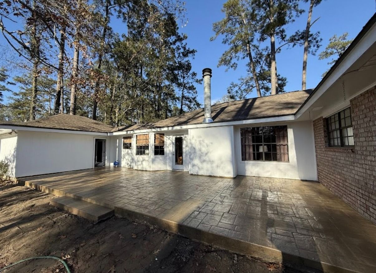 Single-story white house with brick patio and trees in the yard on a sunny day