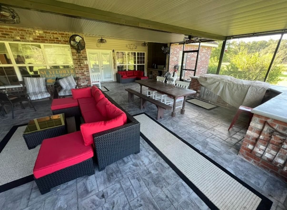 Covered patio with red-and-black wicker seating and a coffee table beside a brick grill area
