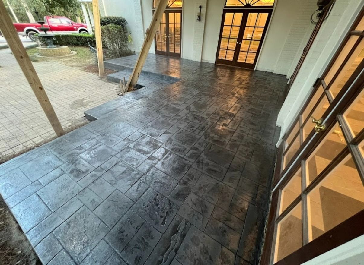 Covered porch with dark stamped concrete floor and wooden support posts beside a glass door.