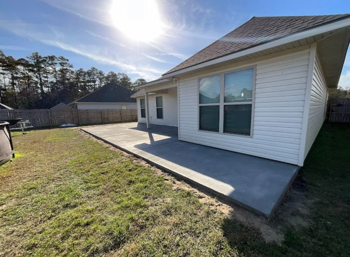 Backyard view of a house with white siding, a concrete patio, and a grassy yard under bright sun.