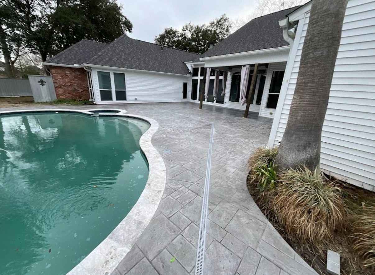 Curved backyard pool beside a white house with a covered patio and palm trees