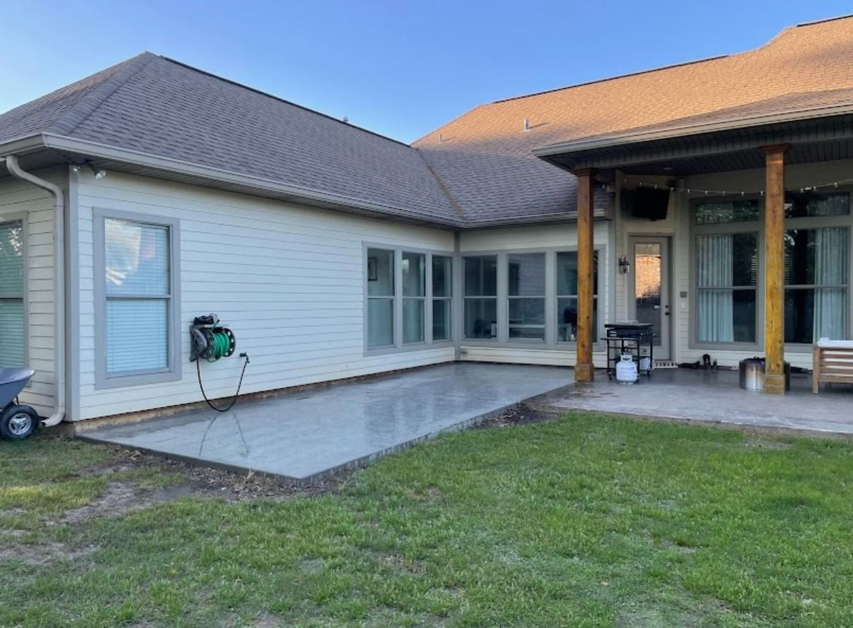 Single-story house patio with white siding, gray roof, green lawn, and covered porch at dusk