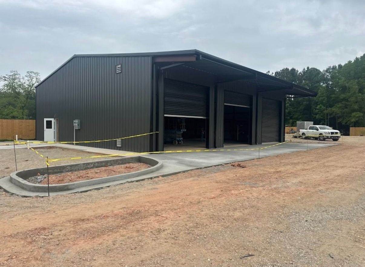 Large black metal warehouse with open bays on a gravel lot, under construction or recently completed.