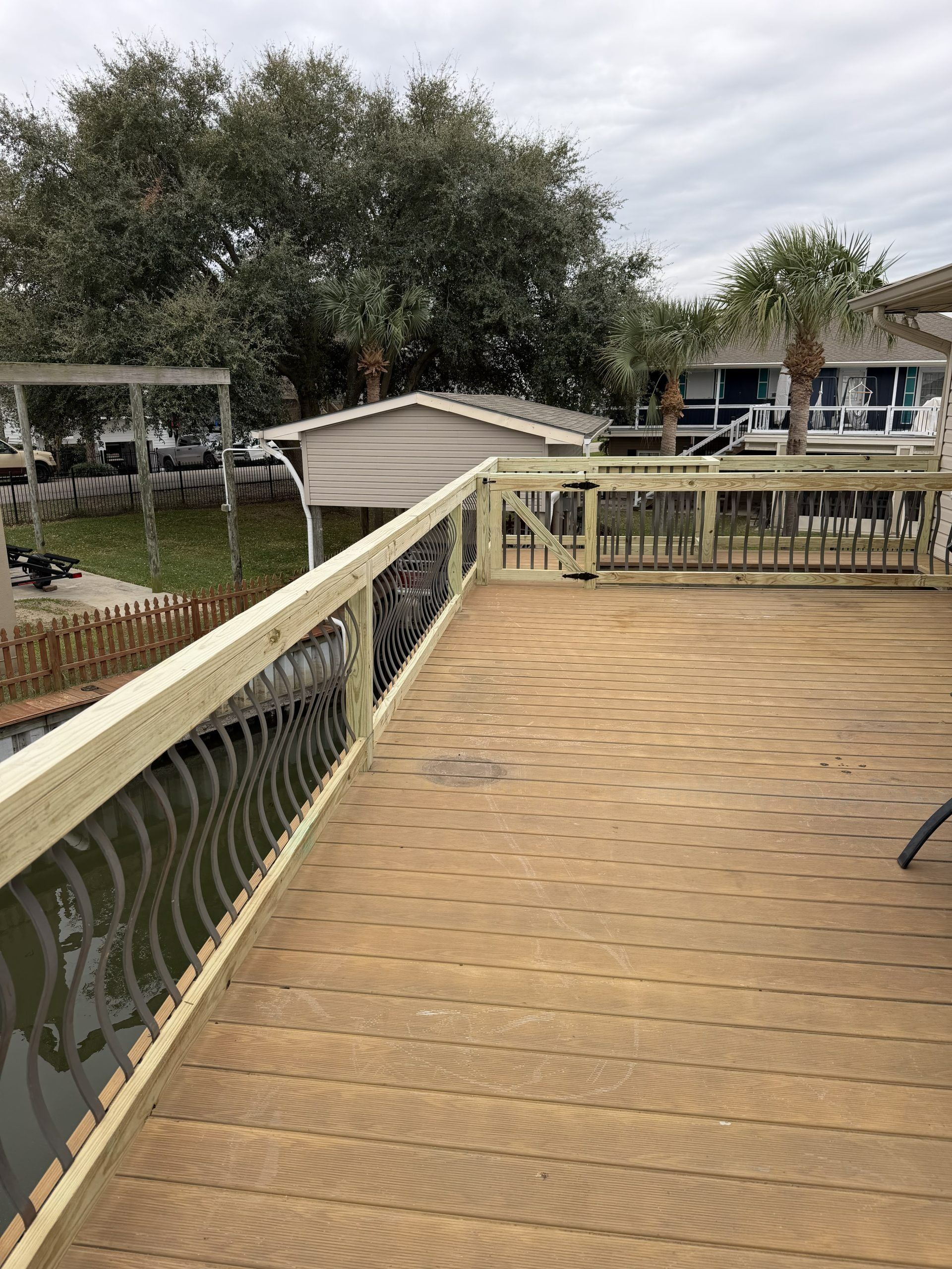 Wooden deck with cream railing overlooking a yard and houses under cloudy sky