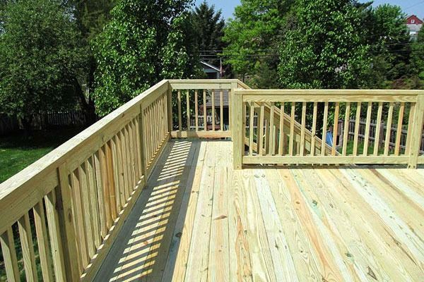 Wooden deck with railings overlooking a green backyard and trees.
