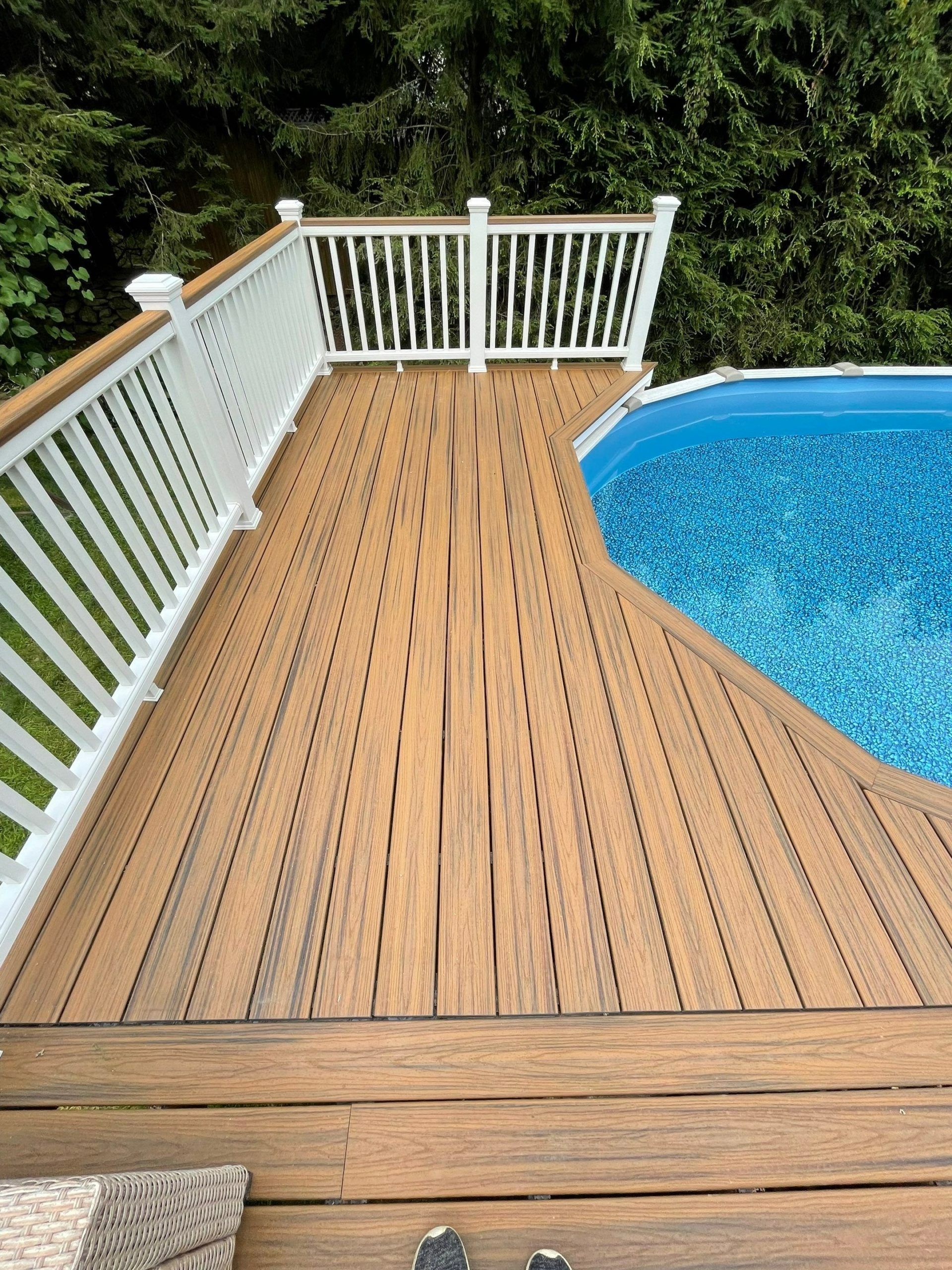 Wooden pool deck with white railing beside a blue swimming pool