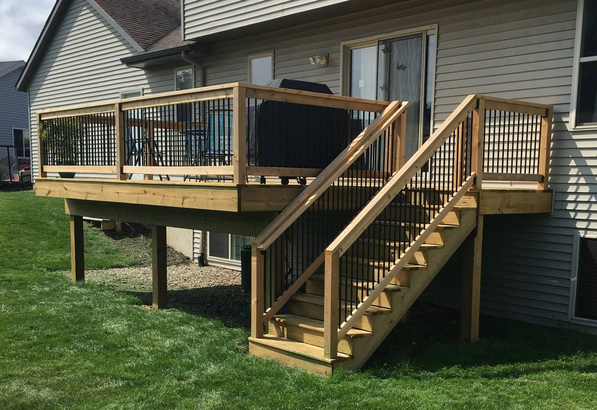 Wooden backyard deck with stairs and railings attached to a house, set over a grassy lawn.