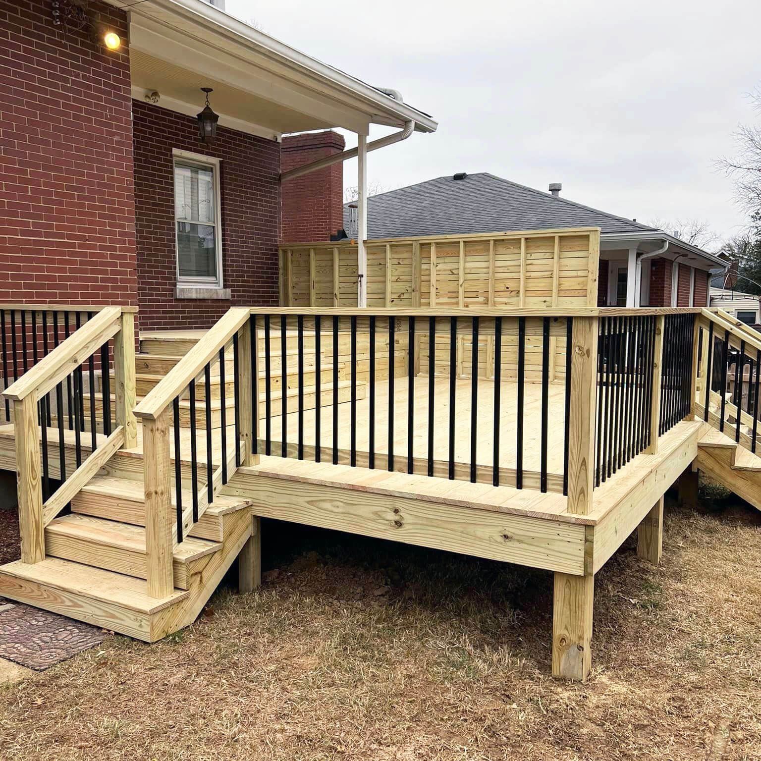 Wooden backyard deck with stairs and railing beside a brick house and fenced yard