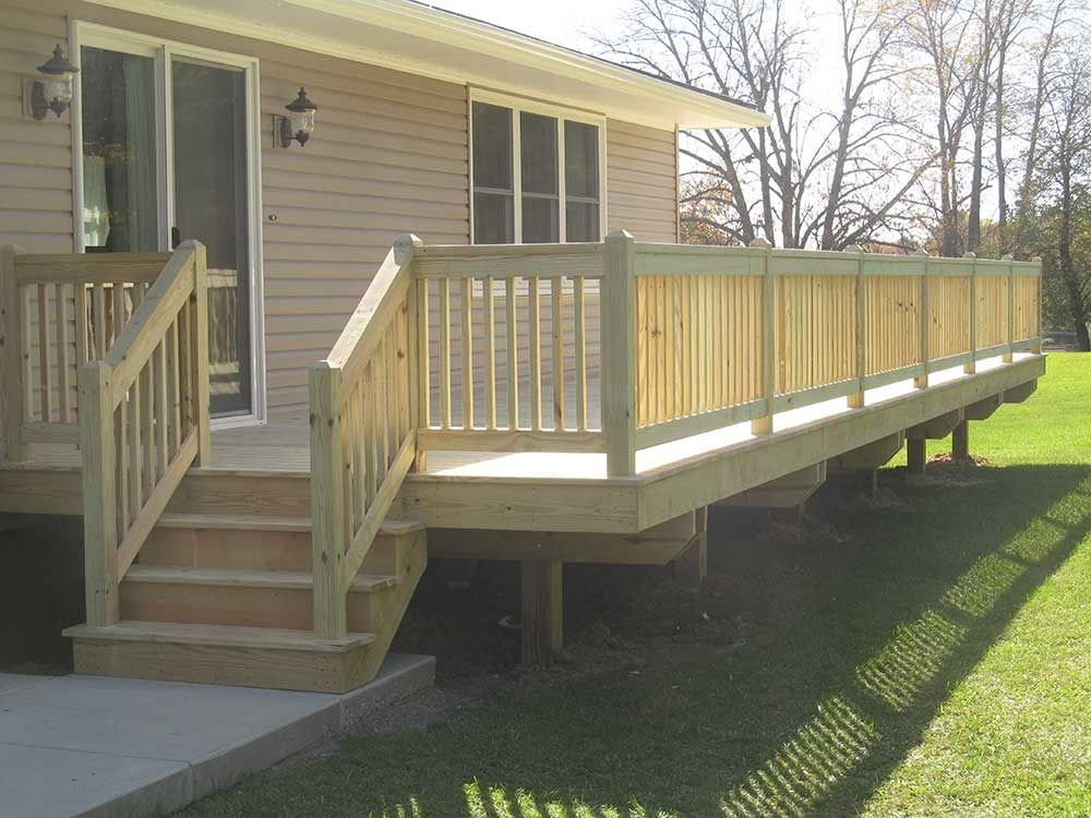 Wooden accessibility ramp with railings leading to a house porch beside front steps.