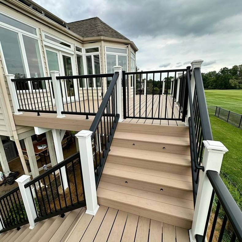 Outdoor staircase with beige steps, black railings, and white siding beside a house deck