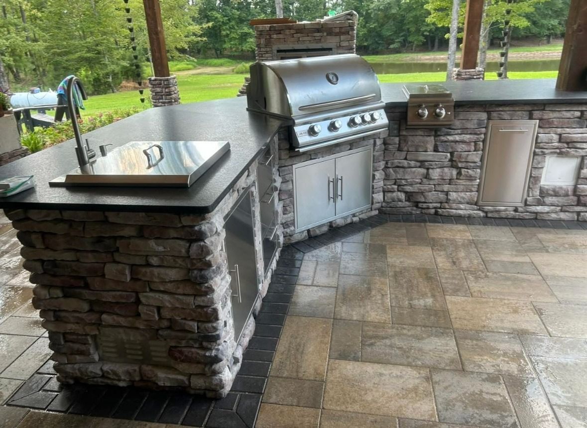 Outdoor stone patio with built-in stainless steel grill and sink under a covered area.