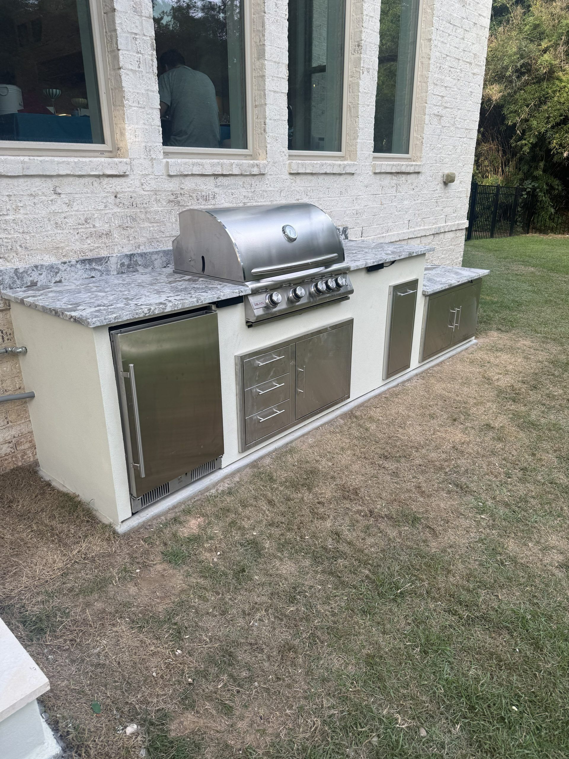Built-in stainless steel grill island beside a house on a gravel patio