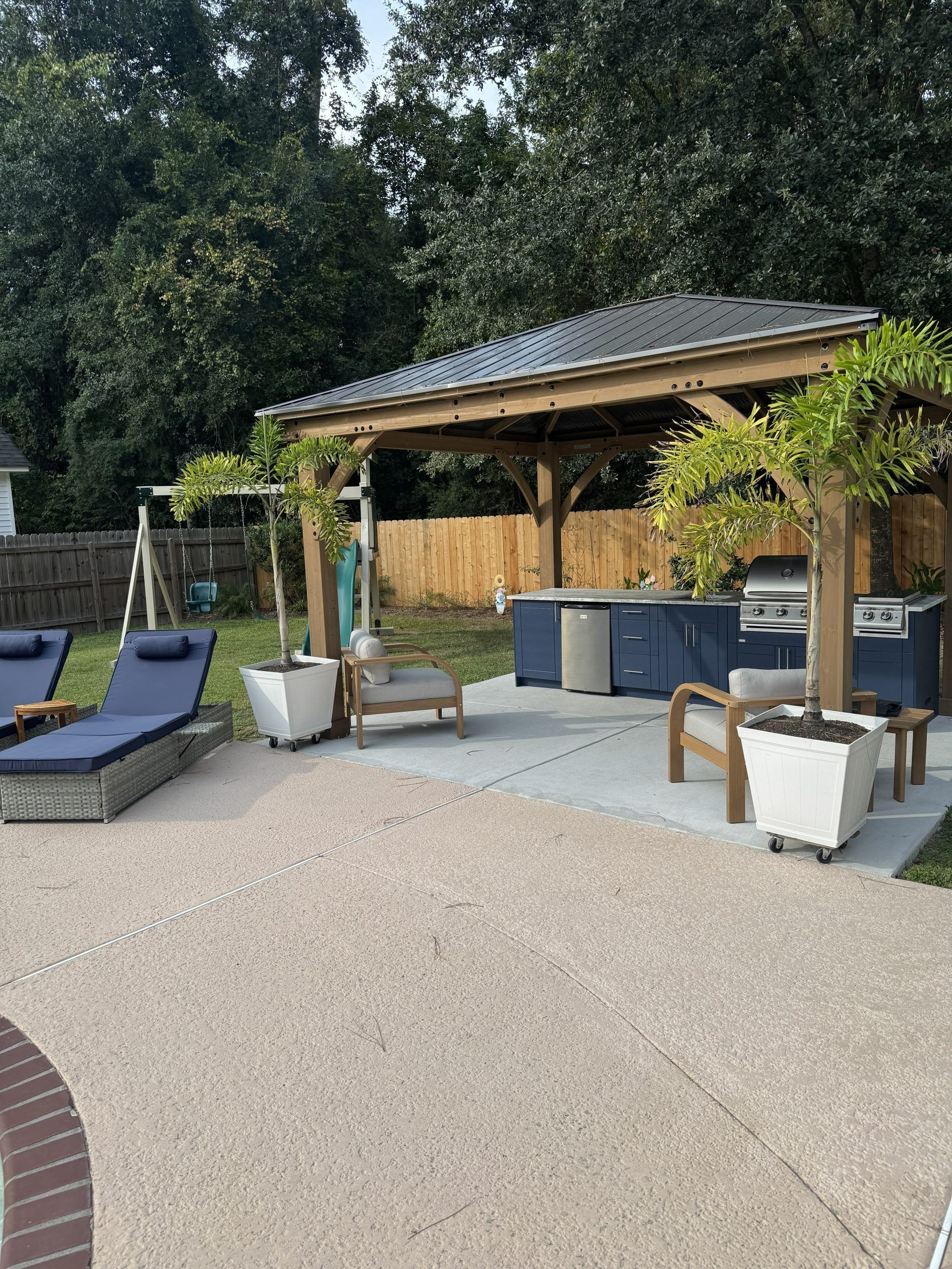Outdoor patio with lounge chairs, potted plants, and a wooden bar under a canopy.