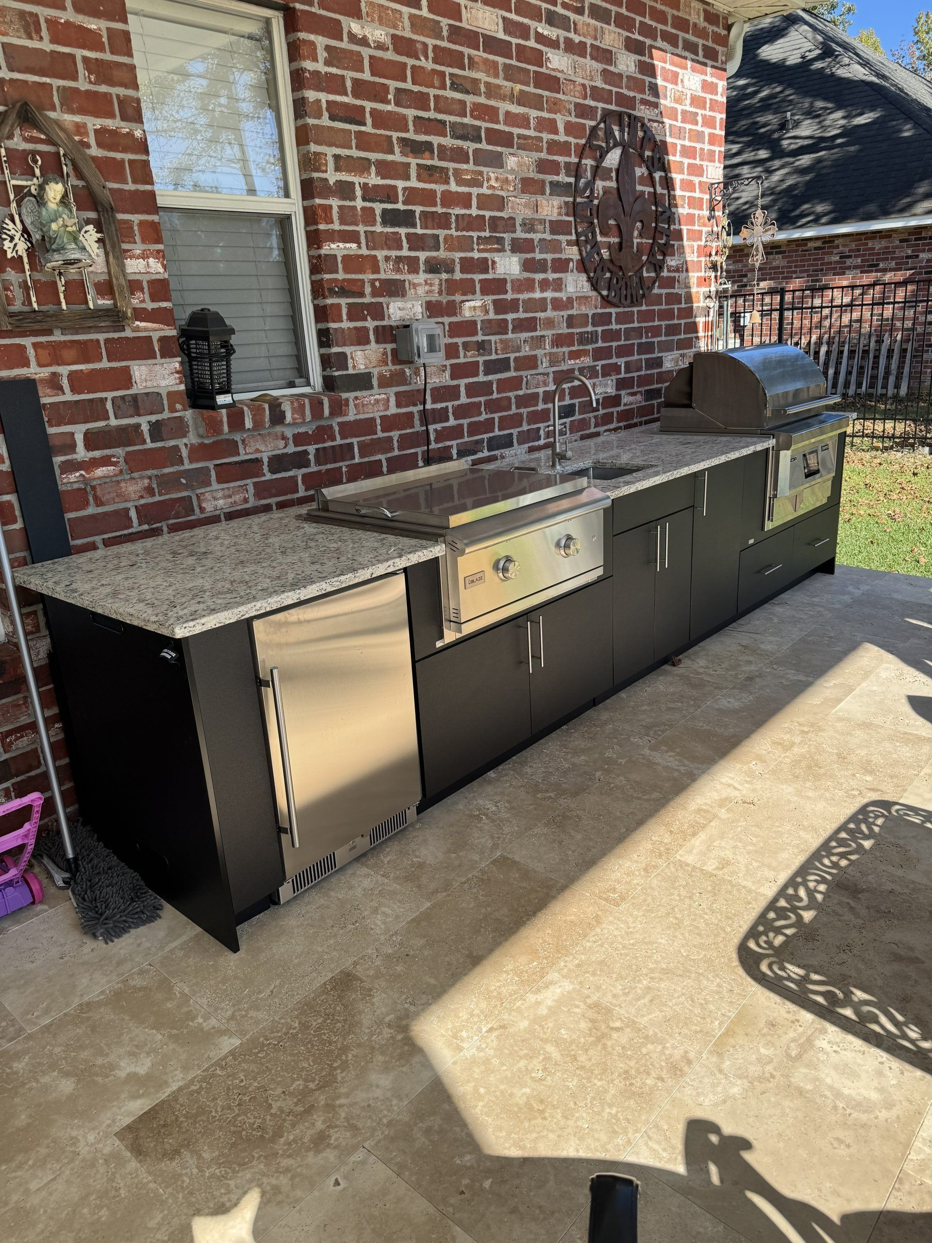 Outdoor black grill and cabinet setup beside a brick house on a concrete patio.