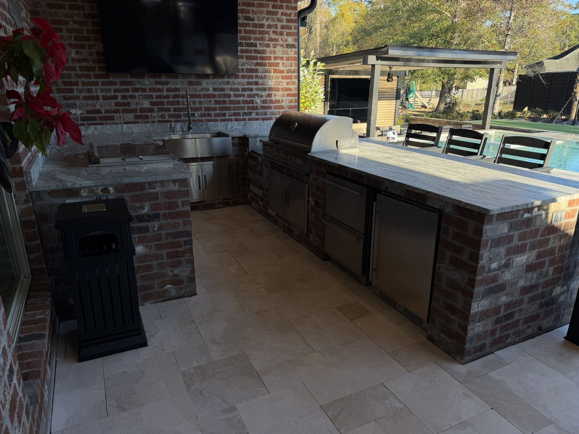 Brick outdoor kitchen with built-in grill, countertop, and black trash bin on a stone patio