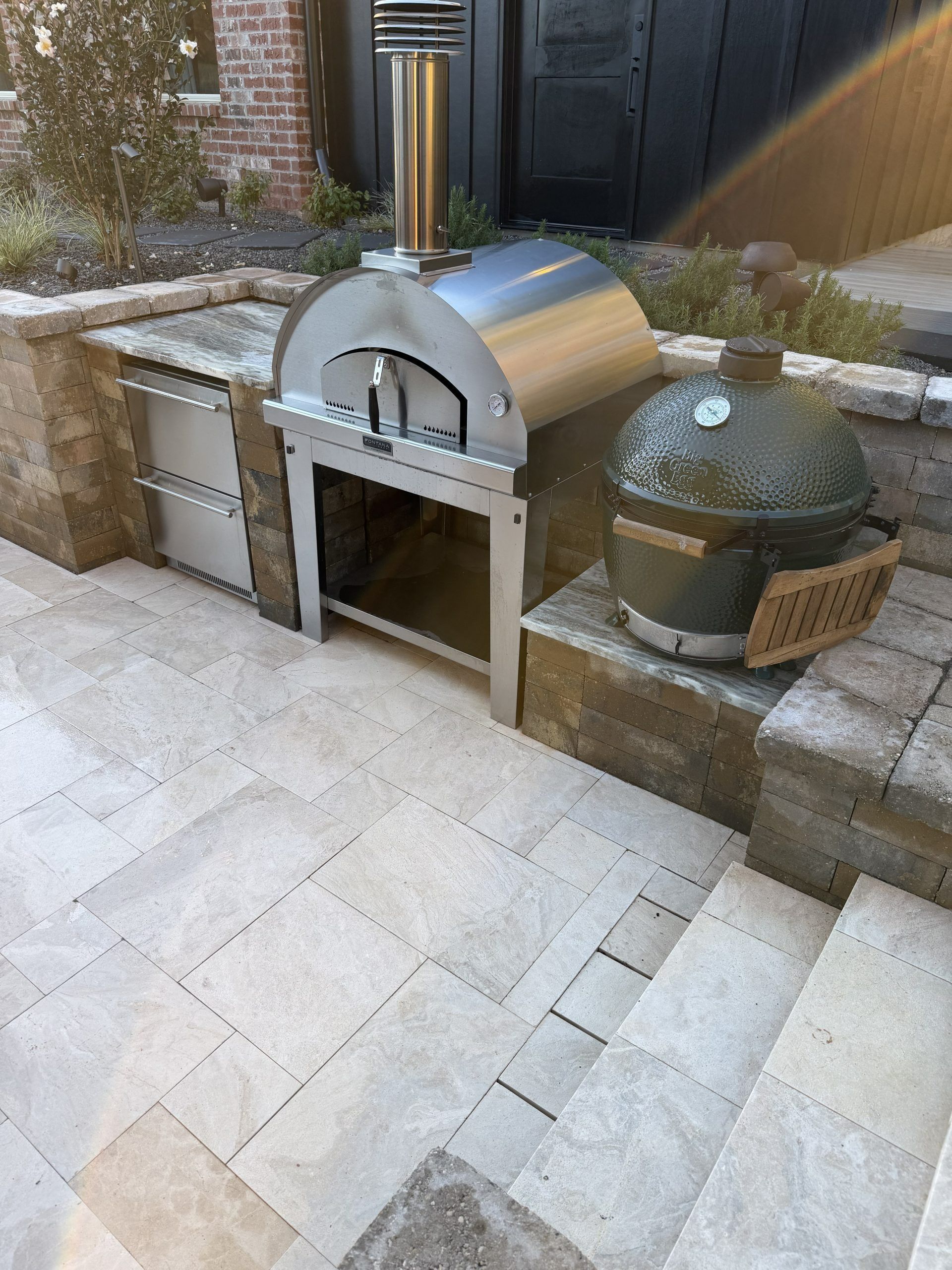 Outdoor stone patio with built-in stainless steel oven, steps, and a covered planter beside a wall