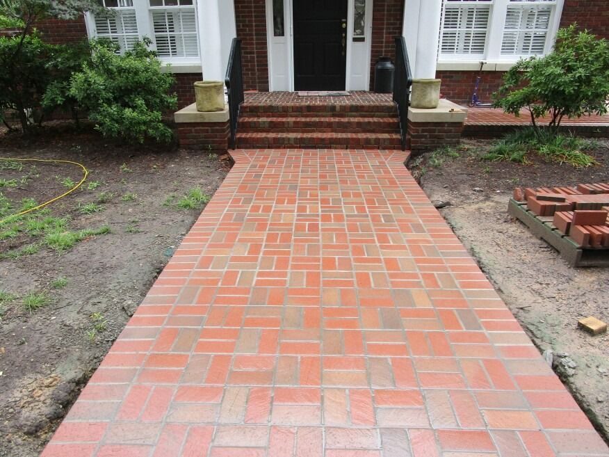 Brick walkway leading to a white house entrance with steps and brick planters on both sides