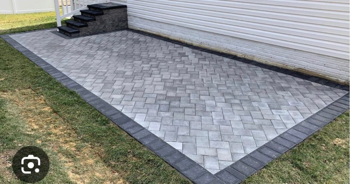 Stone patio beside white house with gray paver border and steps leading up to a door
