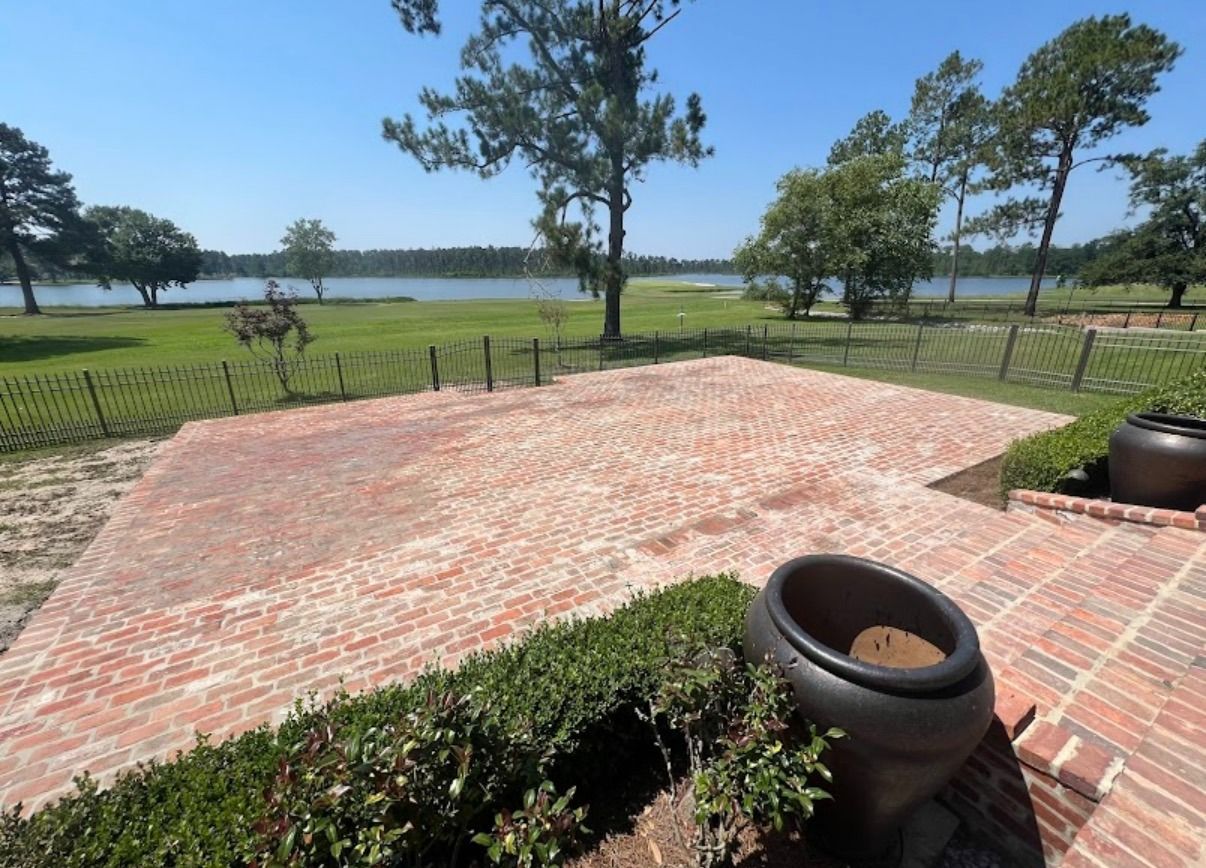 Brick patio overlooking a grassy field and water under a clear blue sky with potted plants in the foreground