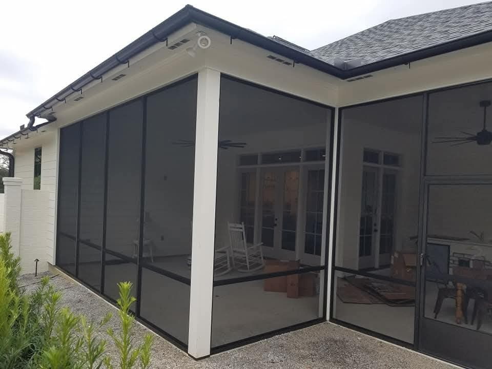 Screened patio attached to a white house with dark trim and a ceiling fan inside