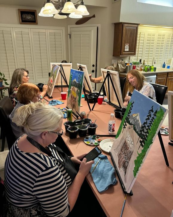 People painting at easels around a table in a bright art class room
