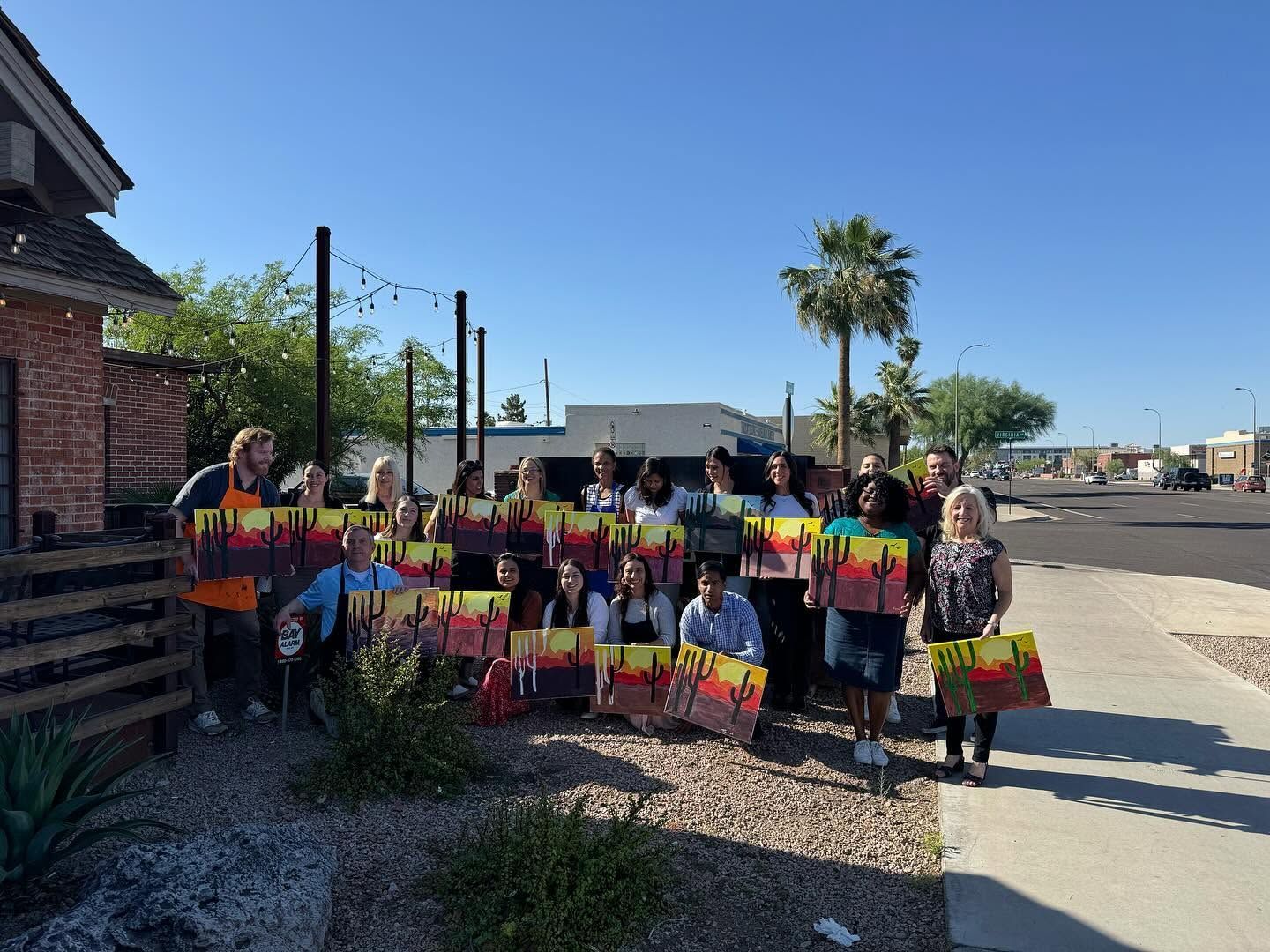 Group holding colorful signs outdoors beside a brick building on a sunny day
