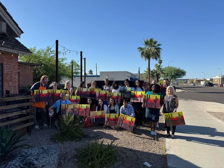 Group holding colorful signs outdoors beside a brick building and roadside under a clear blue sky