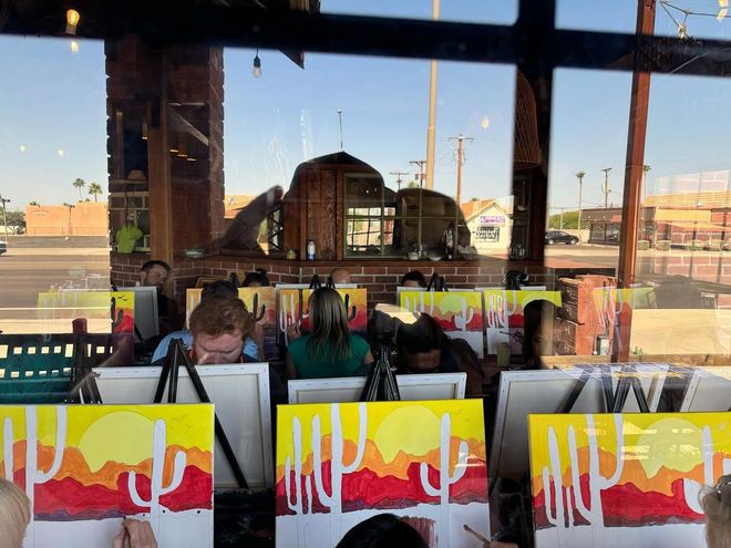 People seated at a cafe window with colorful mural art and an urban street view outside
